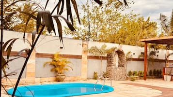 Um deck de madeira com espreguiçadeiras, piscina e um muro de pedra com plantas.