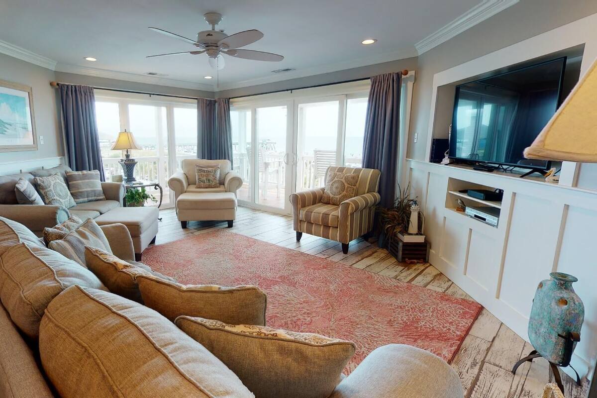 A spacious living room with a large sofa, armchairs, a television, and a ceiling fan.