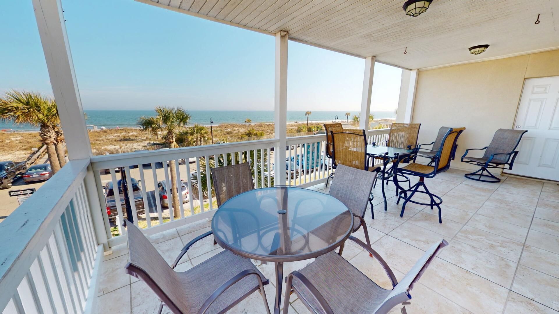 A covered patio with a glass table and chairs, overlooking a beach.