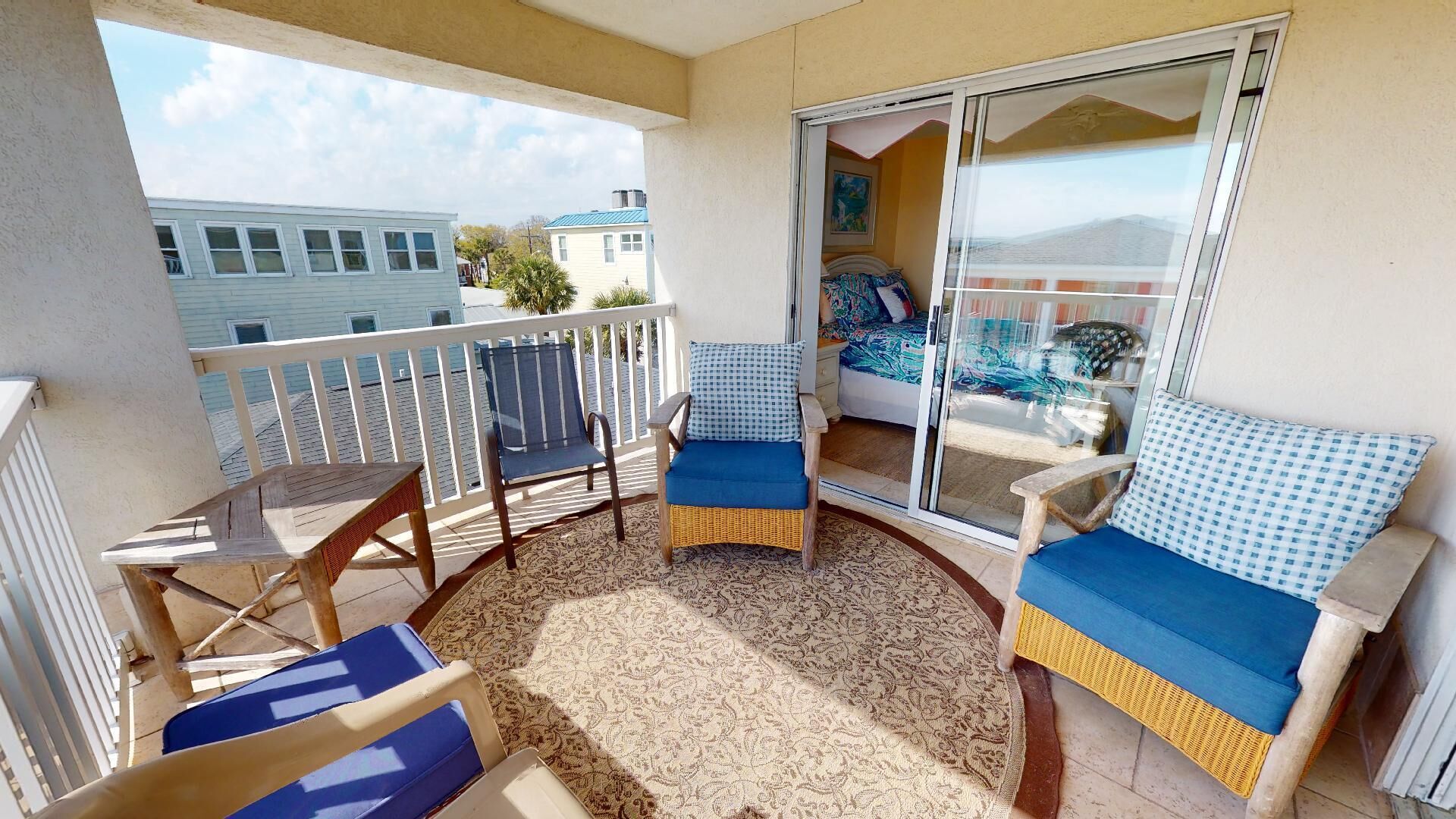 A balcony with a wicker sofa, two chairs, a small table, and a patterned rug.