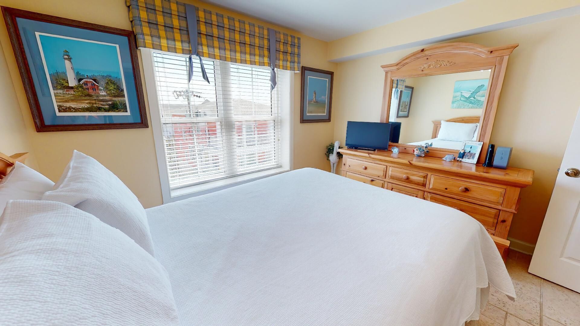 A hotel room with a large bed, a dresser, a television, and a window with blinds.