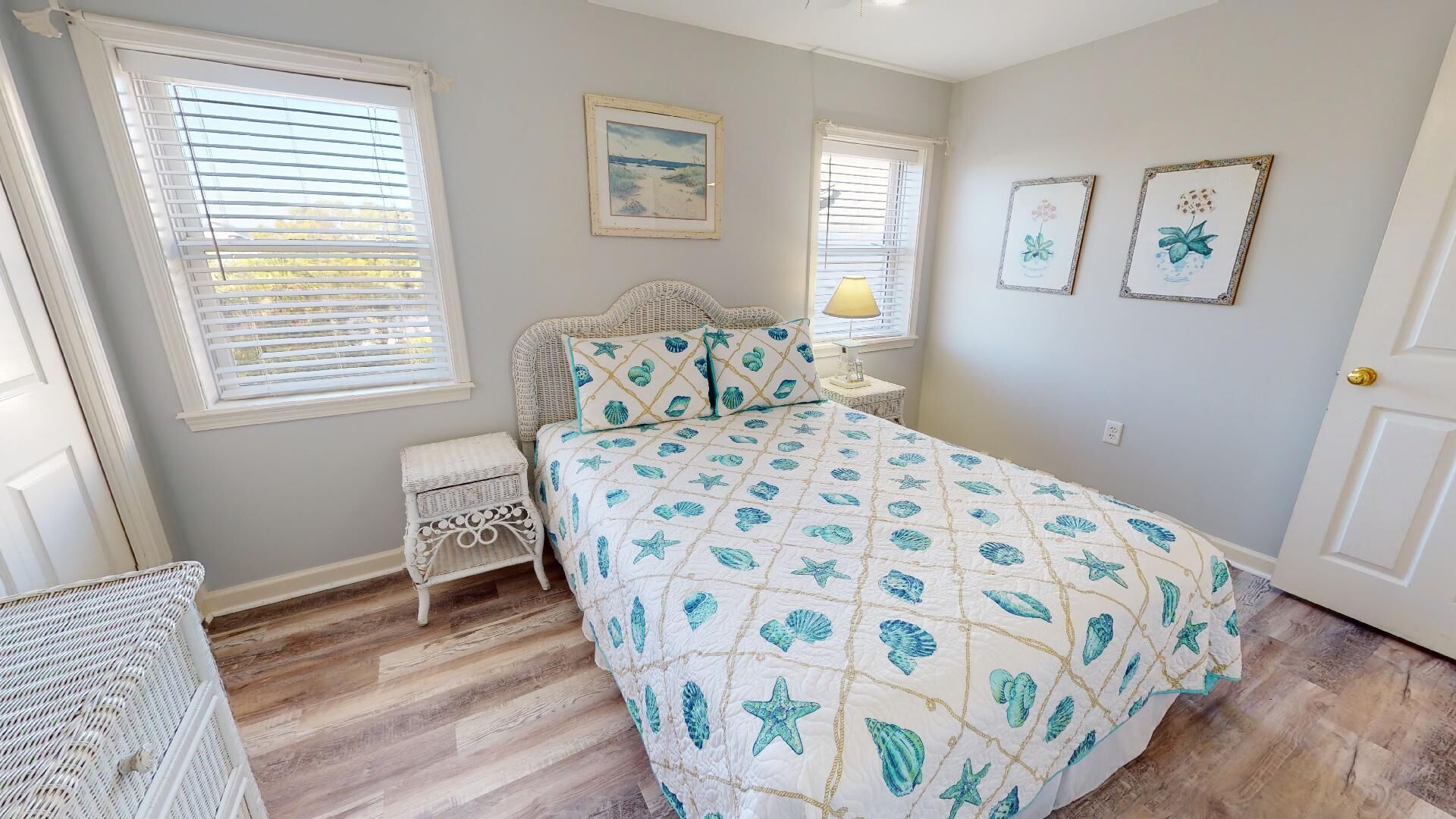 A bedroom with a bed, two windows, a nightstand, a lamp, and wall art.