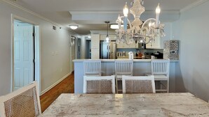 A dining area with a marble table, white chairs, a chandelier, and a kitchen in the background. - Fort Screven Villas Tybee Vacation Rentals (Tybee Island)