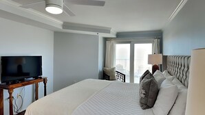 A hotel room with a bed, a television on a wooden table, a ceiling fan, and a view of the outdoors through a sliding door. - Fort Screven Villas Tybee Vacation Rentals (Tybee Island)
