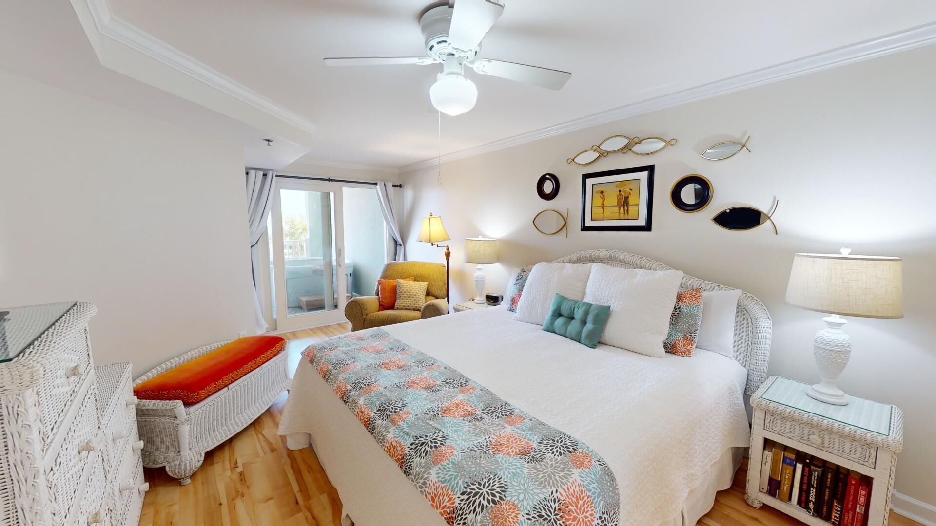 Habitación de hotel con cama, una silla, una mesita con lámpara, estantería y ventilador de techo.
