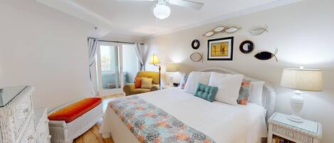 Habitación de hotel con cama, una silla, una mesita con lámpara, estantería y ventilador de techo.
