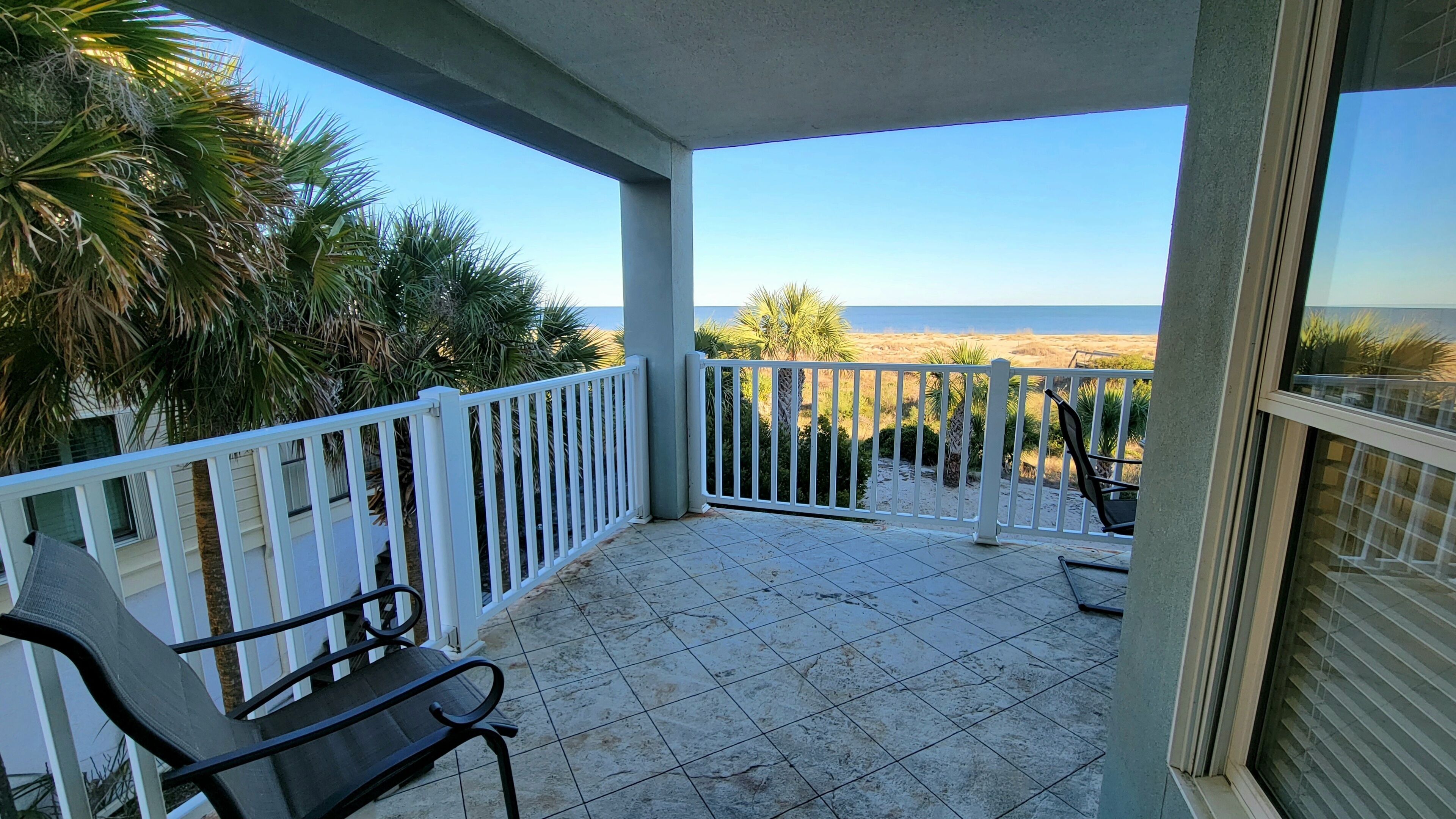 A balcony with a view of the beach, white railings, and a chair.