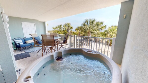 Un jacuzzi sur un balcon avec vue sur des palmiers et une plage de sable.
