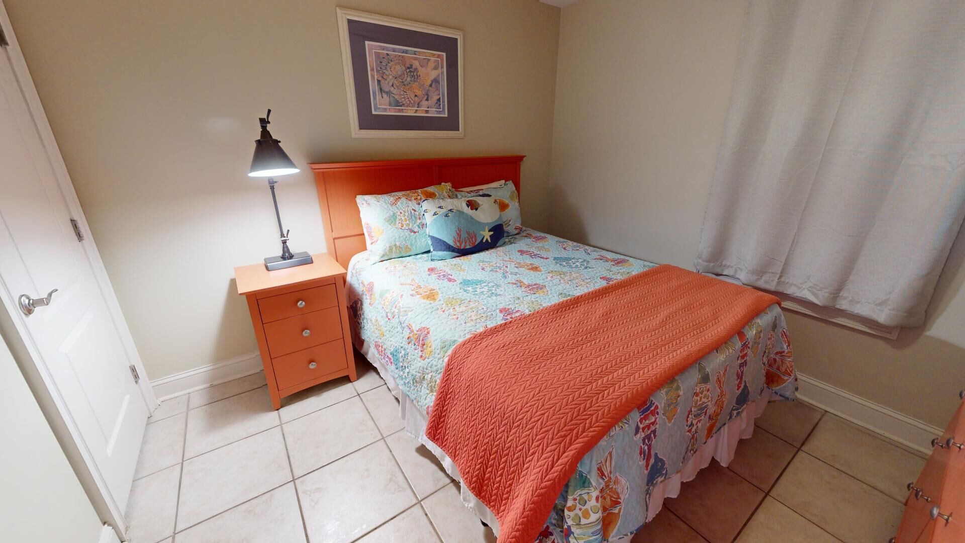 Un dormitorio con cama, mesita de noche, lámpara, un cuadro en la pared y ventana con cortinas.