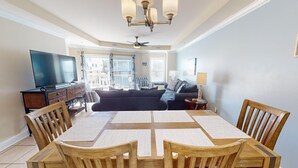 A spacious living room with a dining area, a television, and a balcony with a view. - Gull Reef 614 Tybee Vacation Rentals (Tybee Island)
