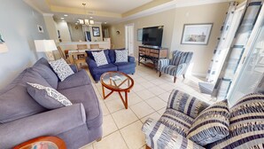 A living room with a sofa, armchairs, a coffee table, and a TV. - Gull Reef 614 Tybee Vacation Rentals (Tybee Island)