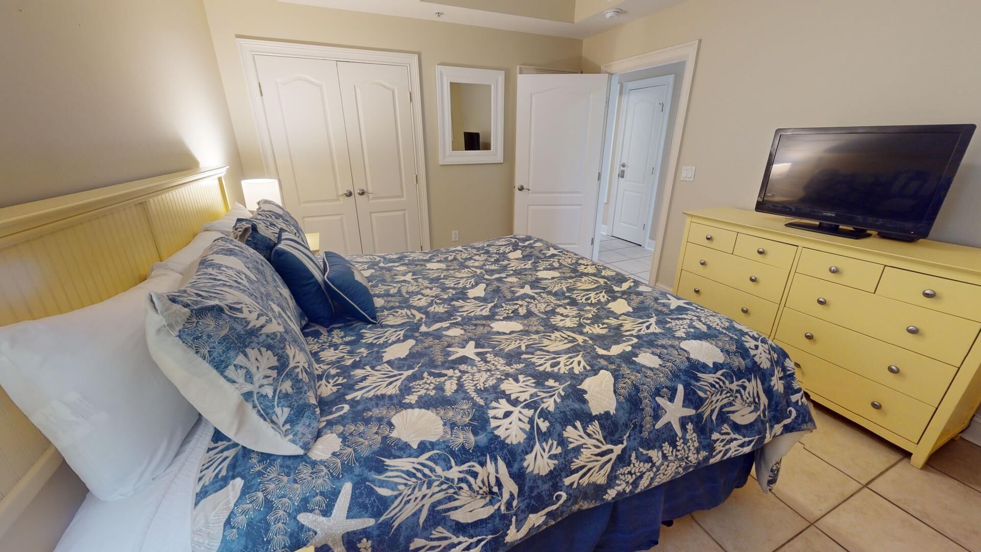 Un dormitorio con cama, cómoda, televisor y dos puertas.