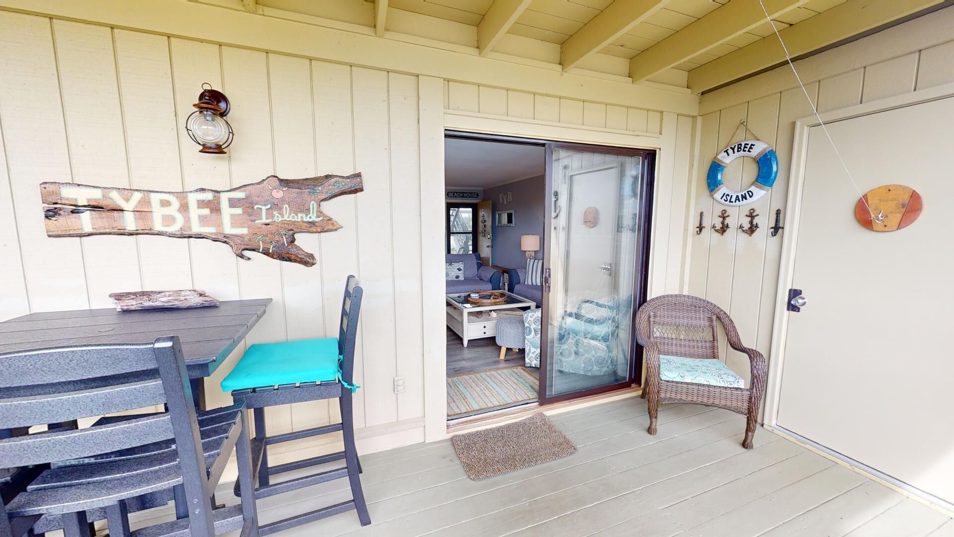 A cozy outdoor seating area with a table and chairs, a wicker chair, and a door leading to a bedroom.