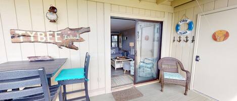 A cozy outdoor seating area with a table and chairs, a wicker chair, and a door leading to a bedroom.