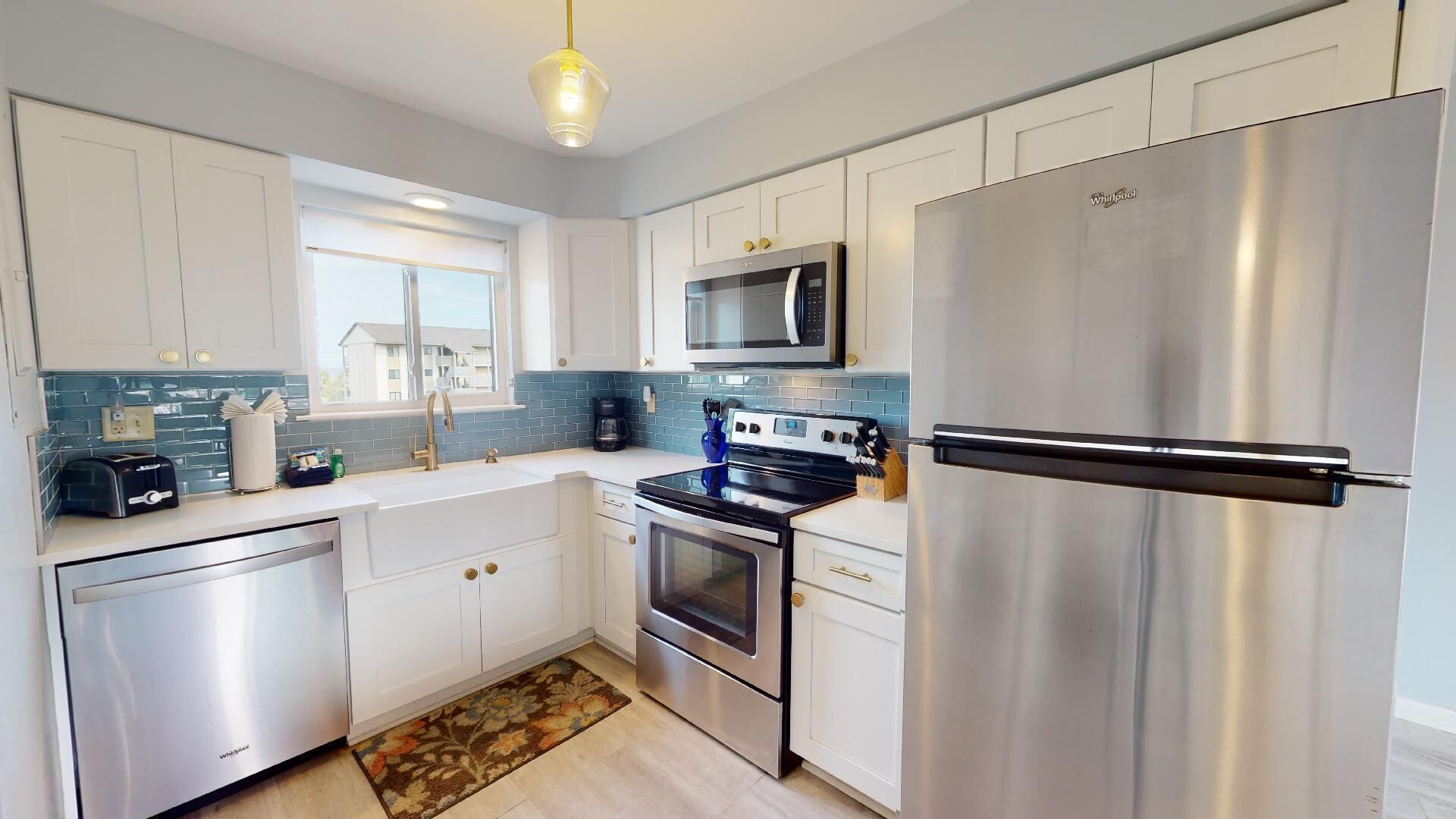 A modern kitchen with stainless steel appliances, white cabinetry, and a blue-tiled backsplash.