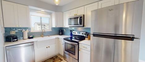 A modern kitchen with stainless steel appliances, white cabinetry, and a blue-tiled backsplash.