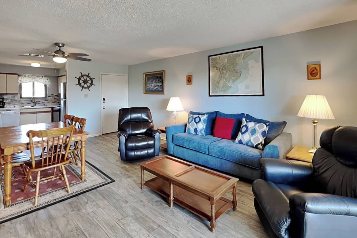 Un salon comprenant un coin repas, un fauteuil en cuir noir, un canapé bleu et une table basse en bois.
