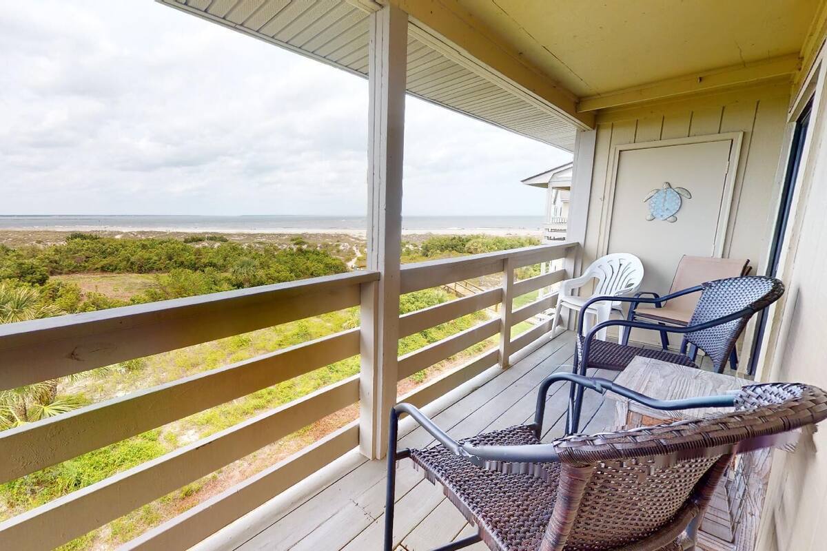 Un balcon donnant sur la plage, des fauteuils en osier et une porte blanche.