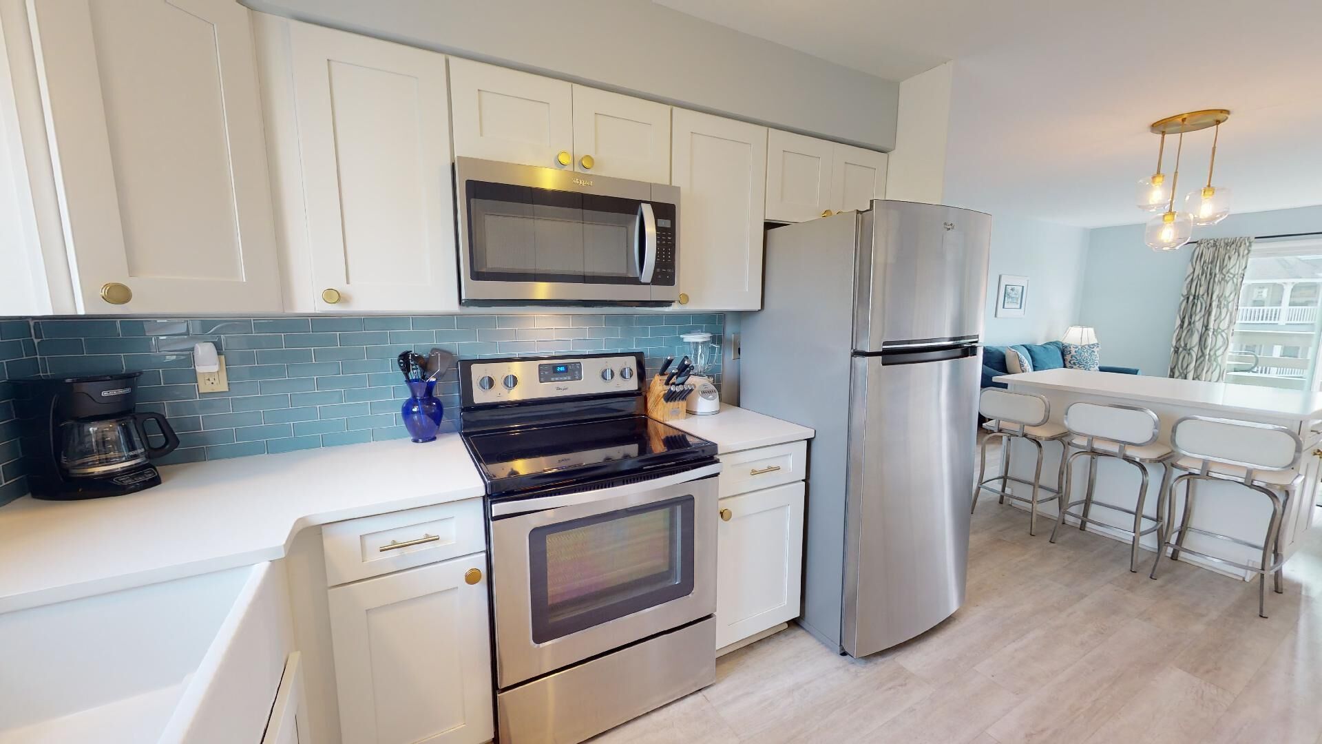 A modern kitchen with white cabinets, a stainless steel refrigerator, a microwave, a stove, and a coffee maker.