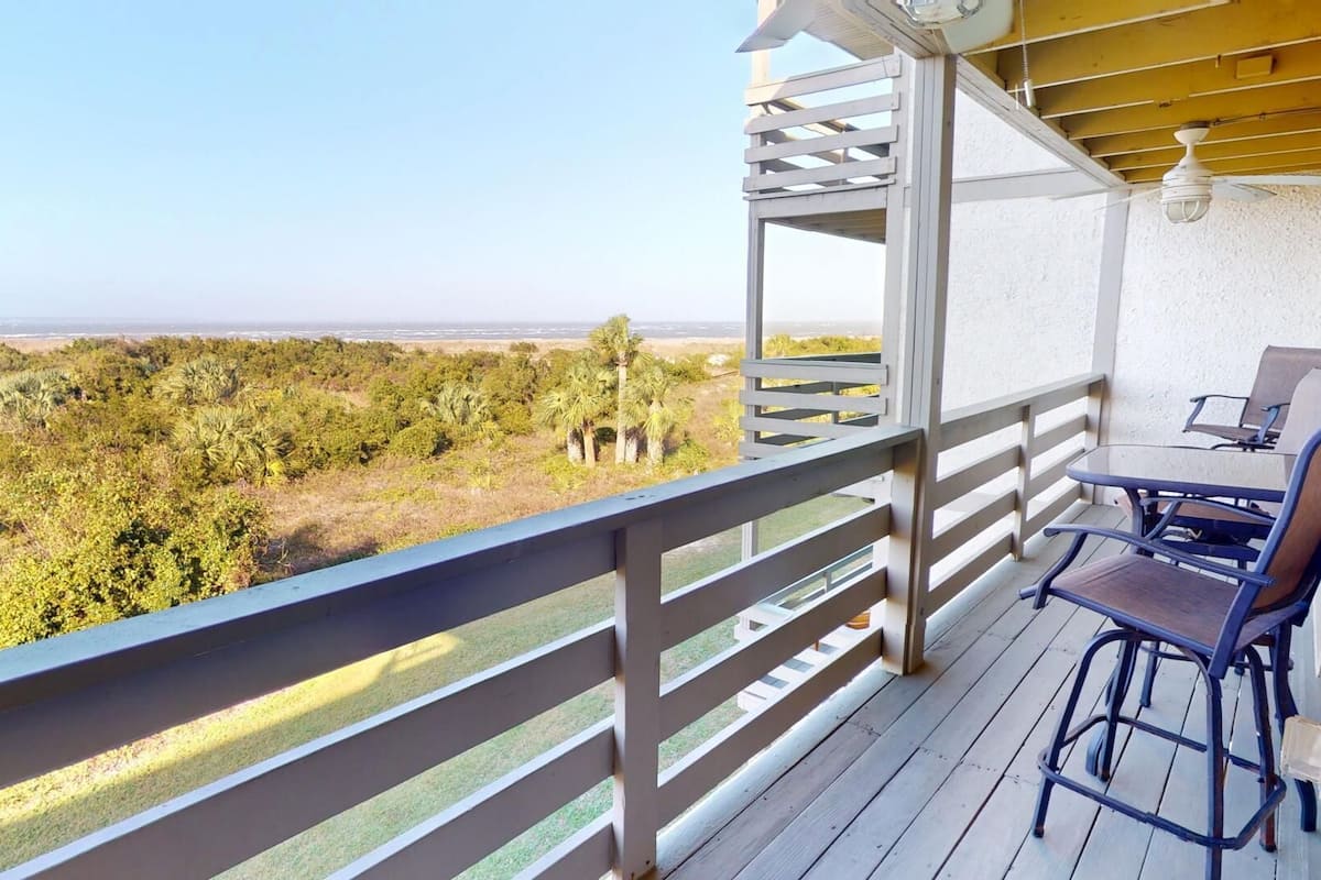 Un balcon avec vue sur l’océan et une table avec des chaises.
