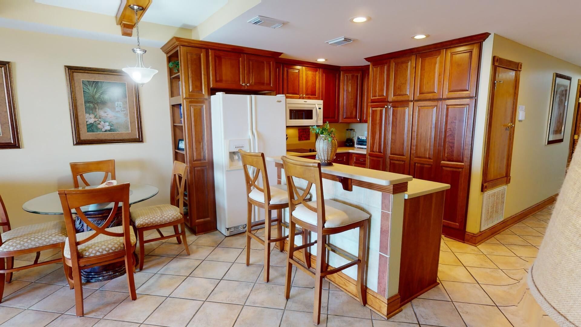 A kitchen with wooden cabinets, a refrigerator, a microwave, and a dining area with chairs and a table.
