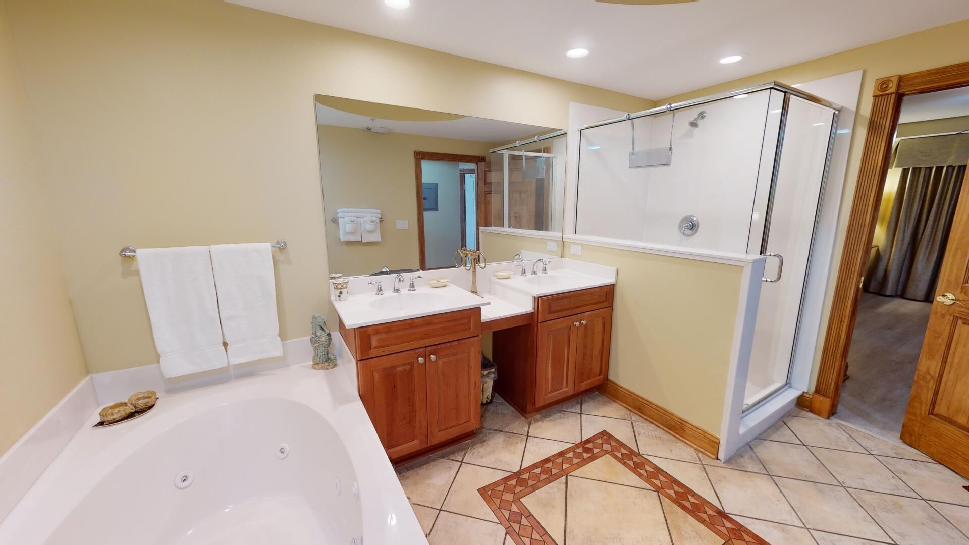A bathroom with a bathtub, two sinks, wooden cabinets, a glass shower enclosure, and a patterned rug.