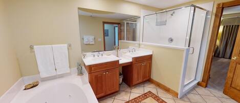 A bathroom with a bathtub, two sinks, wooden cabinets, a glass shower enclosure, and a patterned rug.