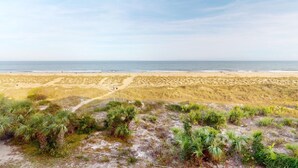 Ein Strand mit einem sandigen Pfad, der zum Wasser führt, umgeben von niedriger Vegetation und Dünen.