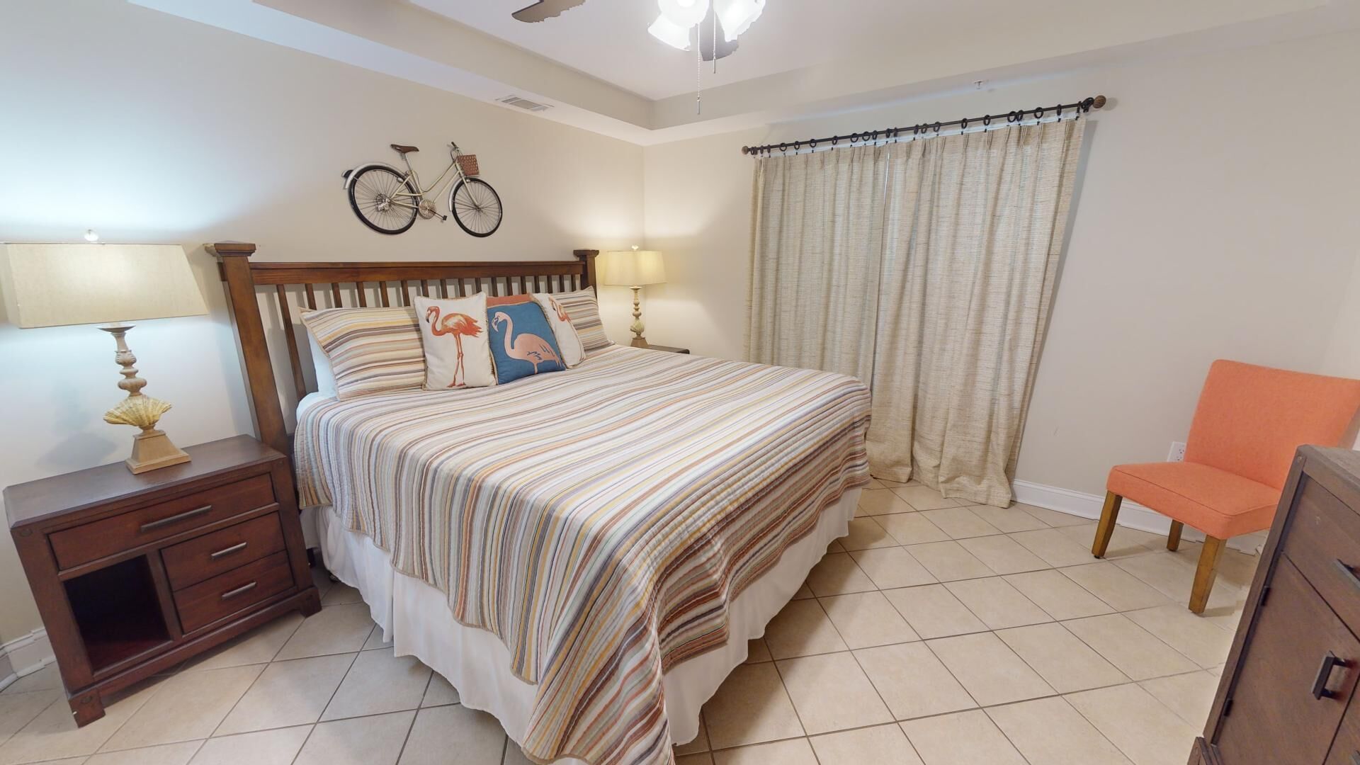 Un dormitorio con una cama grande, dos mesitas de noche con lámparas, una silla y una cortina.