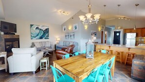 A spacious living area with a wooden dining table, teal chairs, a fireplace, and a kitchen with modern appliances. - Oceanview A by Tybee Vacation Rentals (Tybee Island)