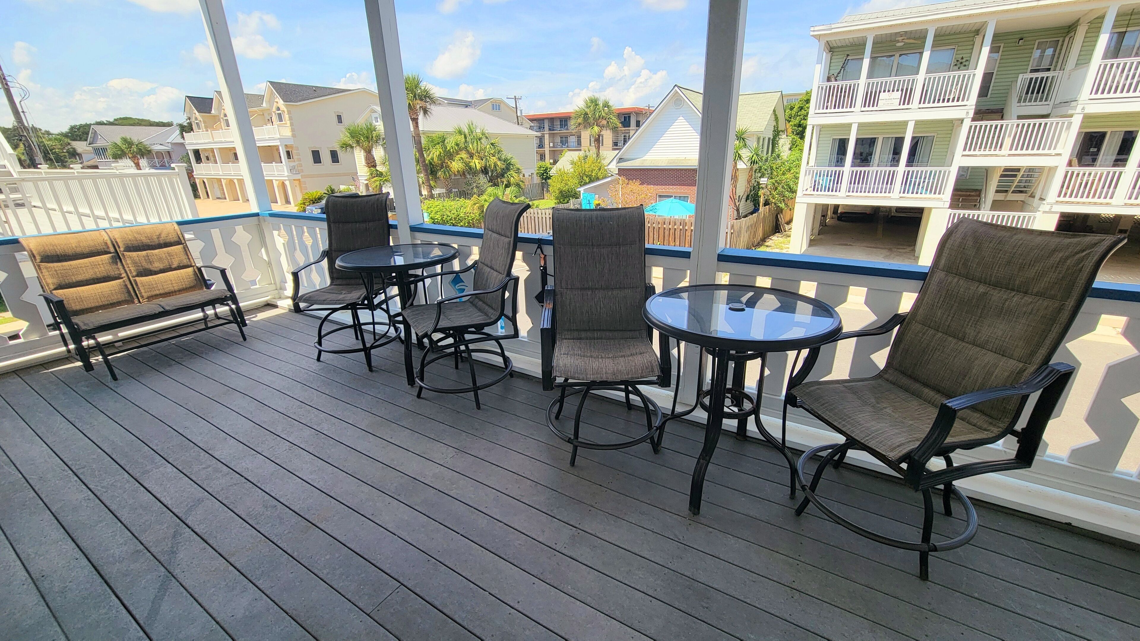 Une terrasse en bois, agrémentée de mobilier d’extérieur, notamment d’un banc et de chaises, qui offre une vue sur un quartier résidentiel avec ses maisons et ses balcons.