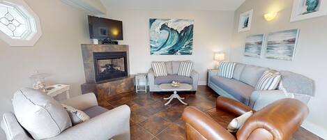 A living room with a fireplace, a television, and a large wave painting on the wall.