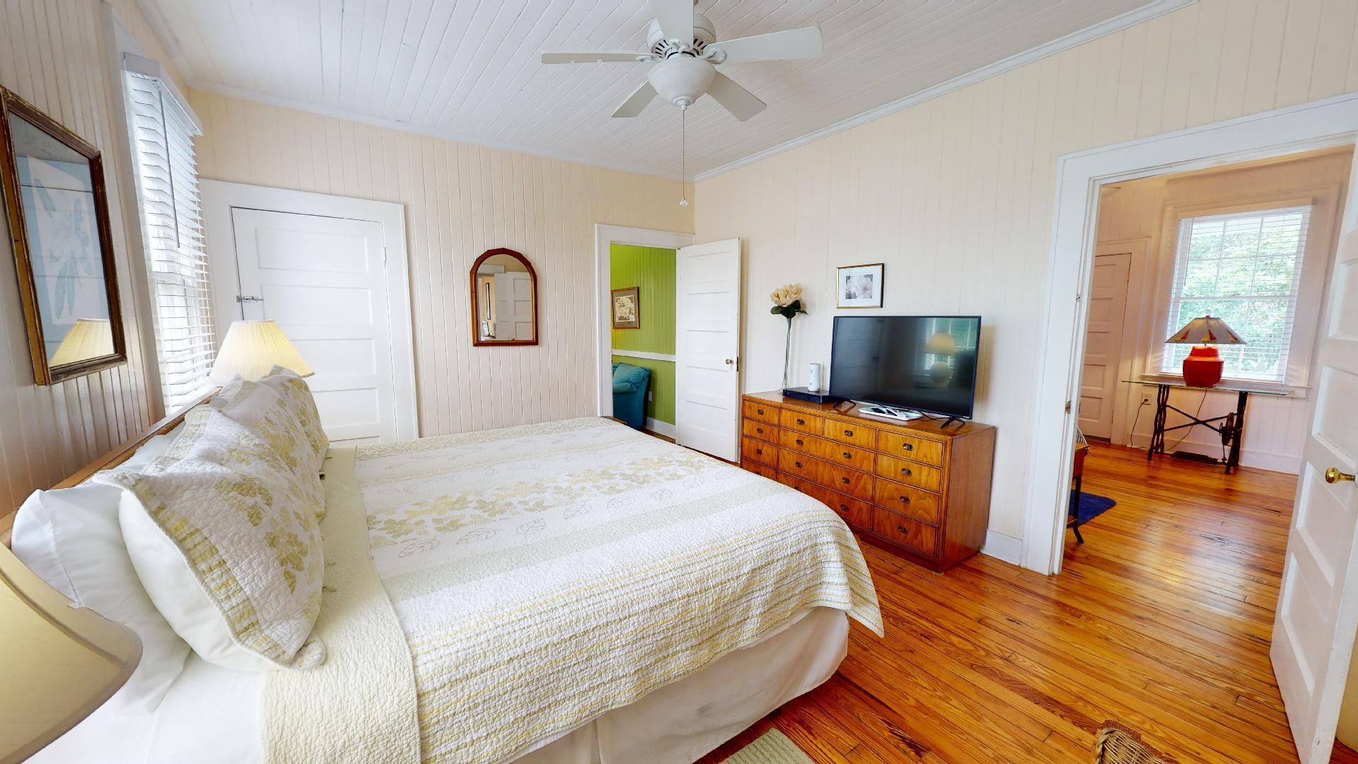 A bedroom with a bed, dresser, television, and a door leading to another room.