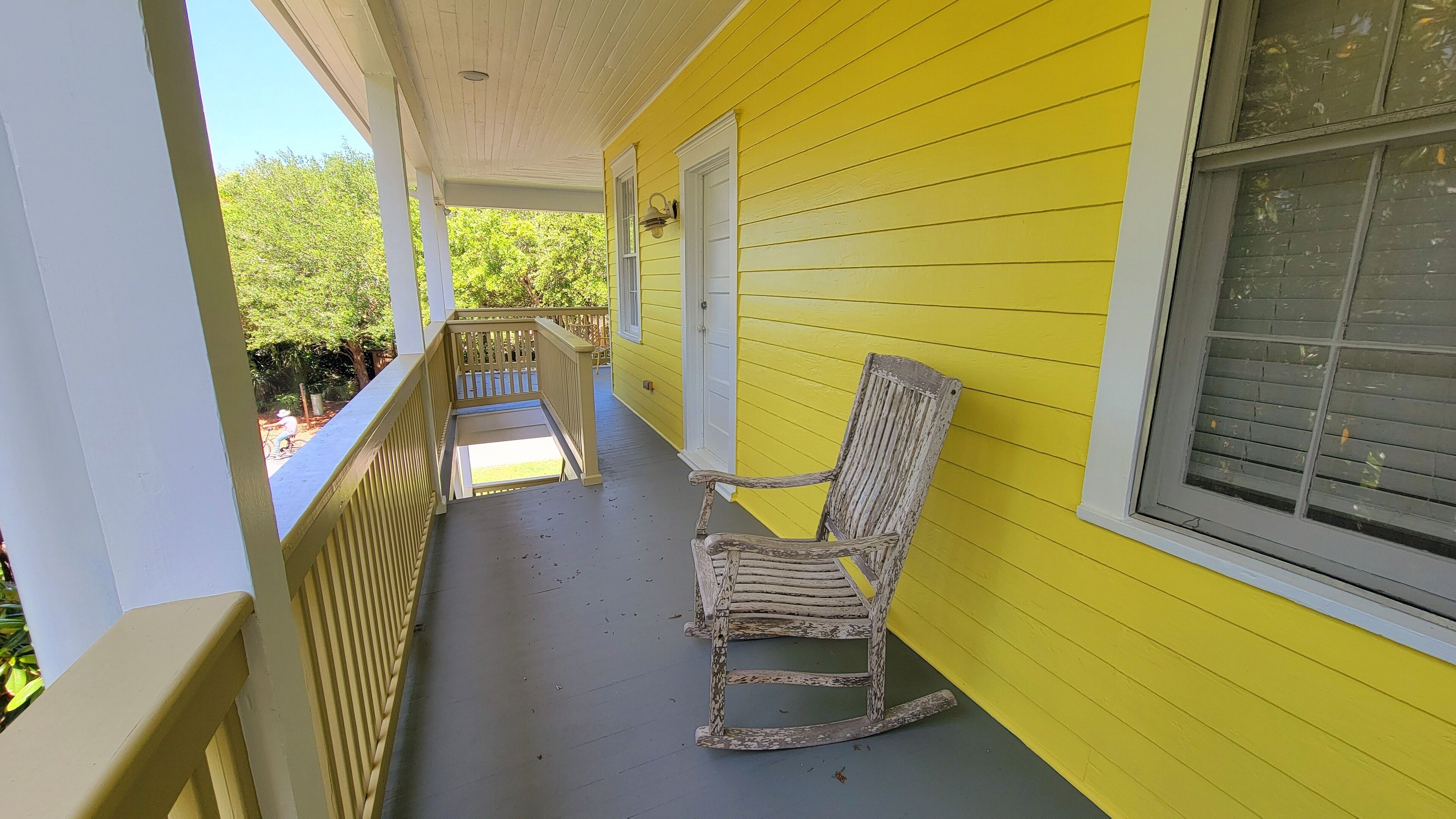 Une véranda avec un fauteuil à bascule, une balustrade blanche et un mur jaune.