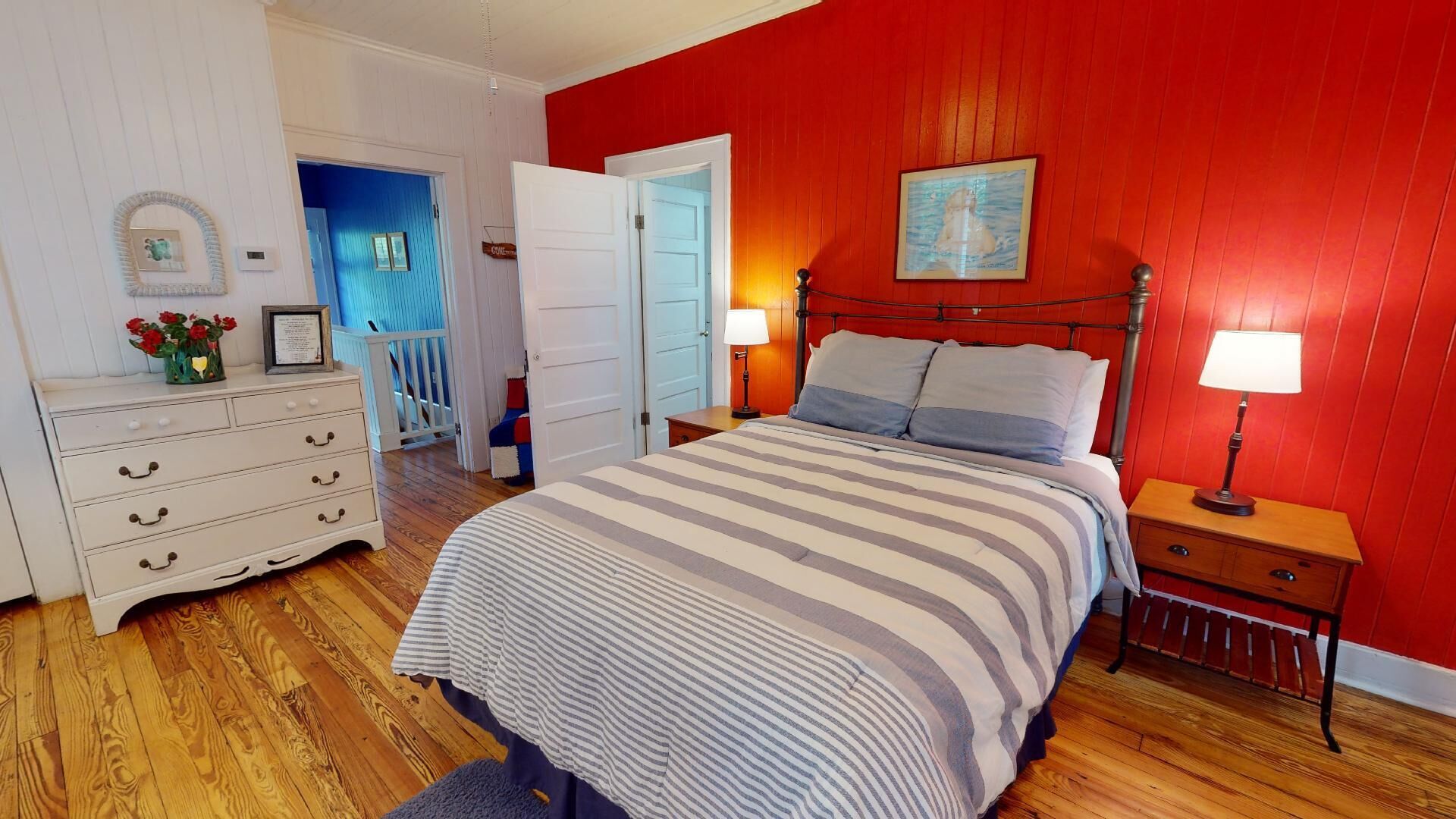 Quarto com cama, cômoda, mesas de cabeceira e uma parede com detalhes em vermelho.