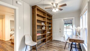 Ein Zimmer mit Holzregal, Deckenventilator, Esstisch mit Stühlen und einem Fenster mit Tageslicht.