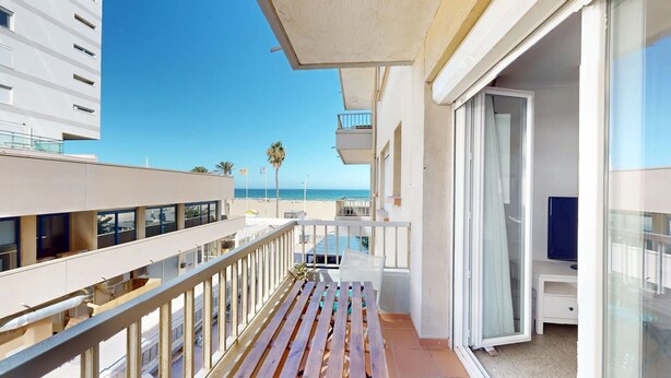A balcony with a view of the beach, a glass door, and a small outdoor seating area.
