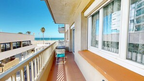 A balcony with a view of the beach, a table with chairs, and a railing.