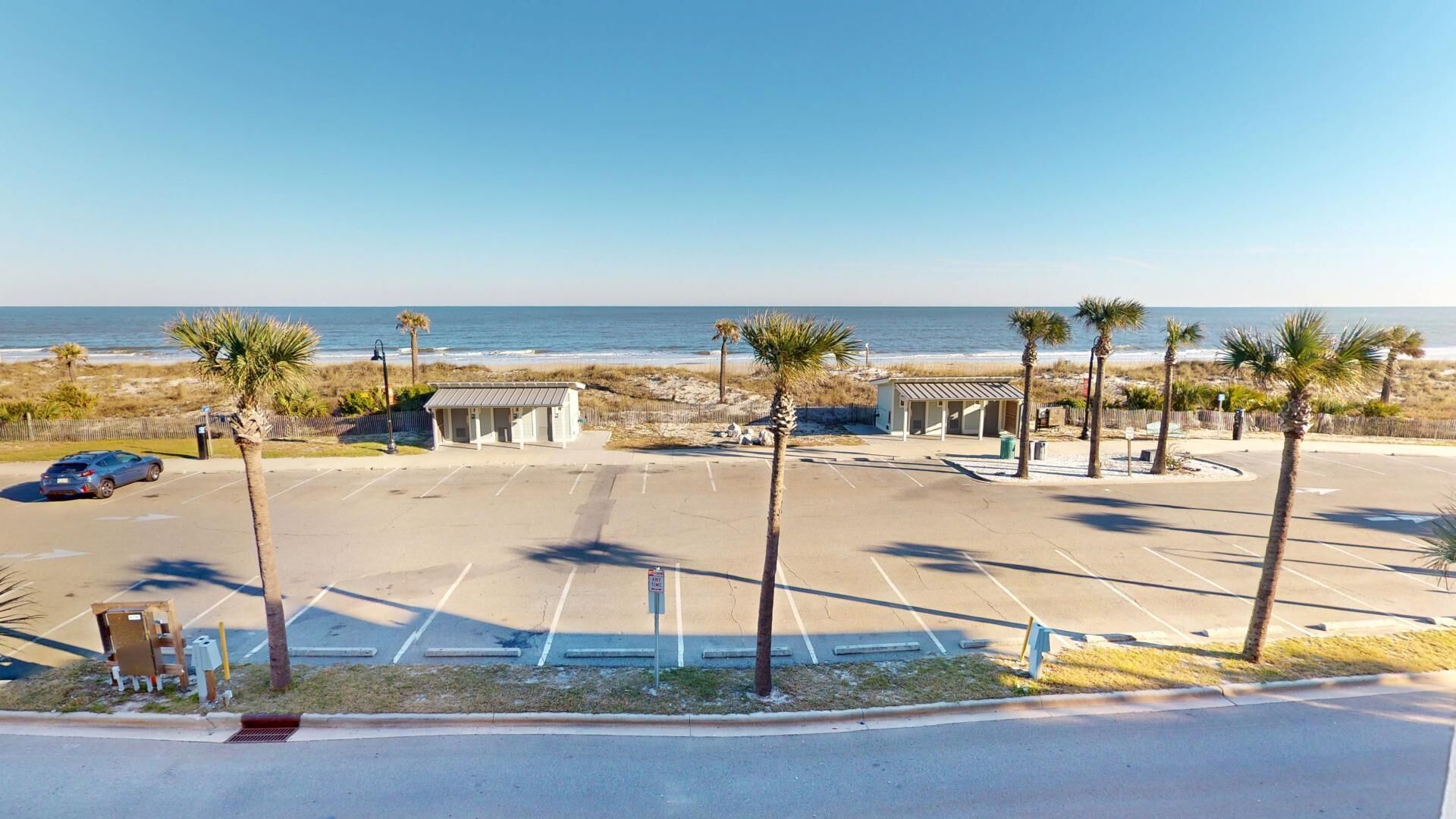 Un estacionamiento con vista al mar, palmeras y un pequeño edificio.
