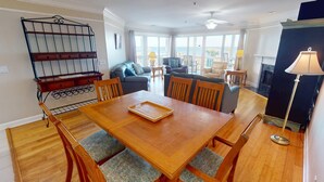 A dining area with a wooden table and chairs, a metal rack, and a view of the ocean through large windows. - Pelican Point by Tybee Vacation Rentals (Tybee Island)