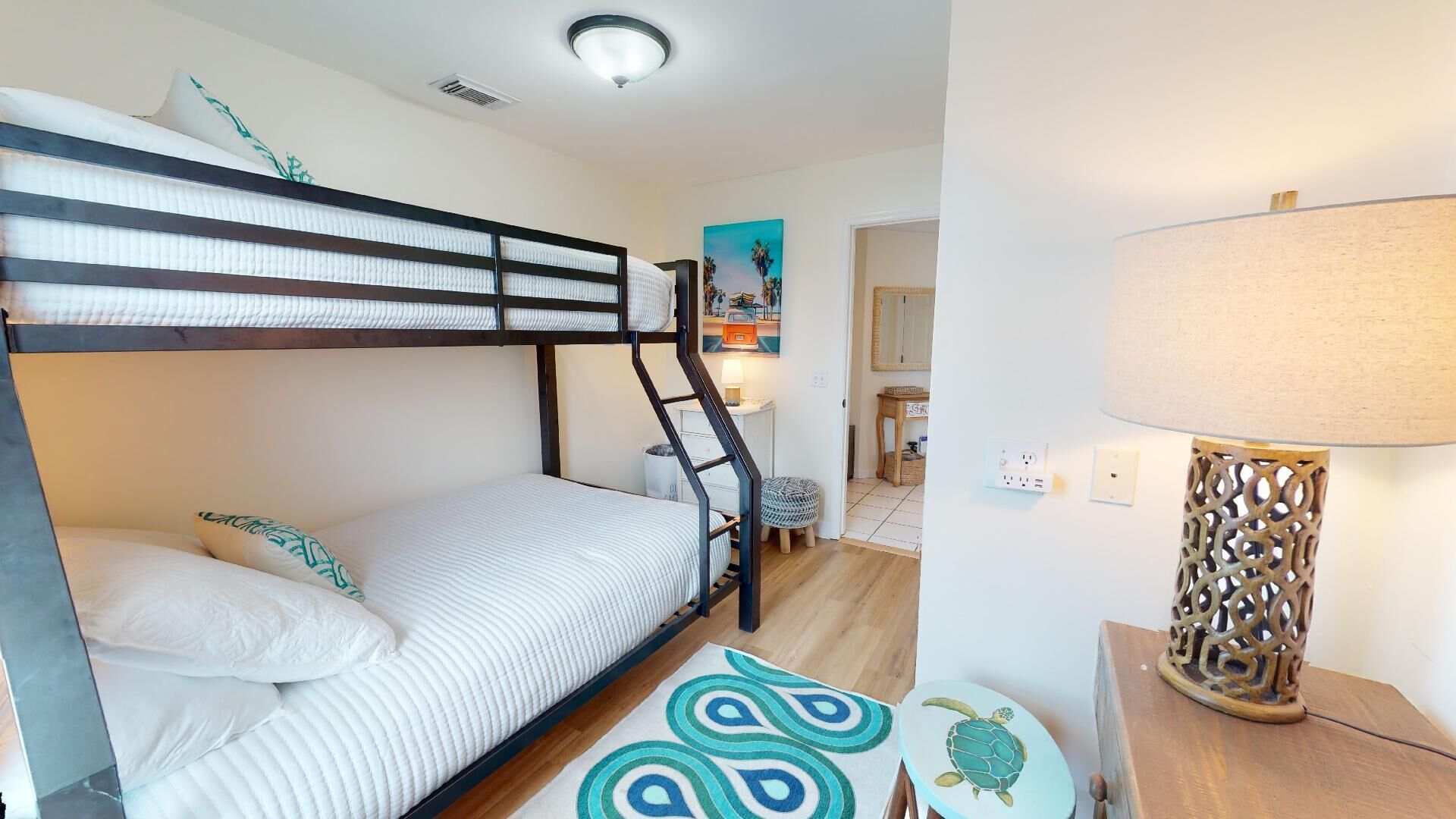 A bunk bed room with a ladder, a small stool, a lamp, and a painting on the wall.