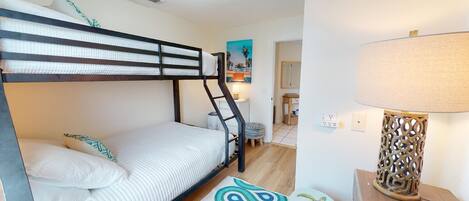 A bunk bed room with a ladder, a small stool, a lamp, and a painting on the wall.