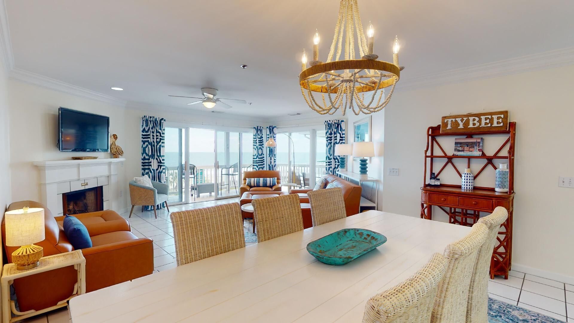 A spacious living room with a large white table, comfortable seating, a fireplace, and a view of the ocean.