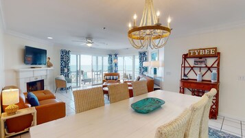 A spacious living room with a large white table, comfortable seating, a fireplace, and a view of the ocean.