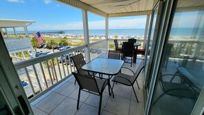 Un balcon fermé avec une porte vitrée, une table, des chaises et une vue sur la plage et la jetée.
