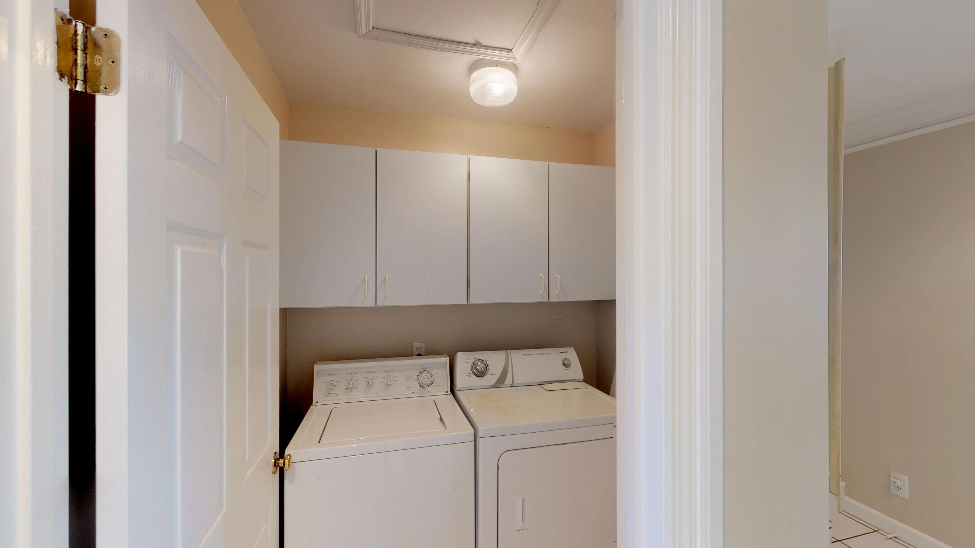 A laundry room with a washer and dryer, white cabinets, and a ceiling light fixture.