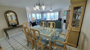 A dining area with a glass-top table, wooden chairs, and a view of the sea through large windows. - Pelican Point by Tybee Vacation Rentals (Tybee Island)