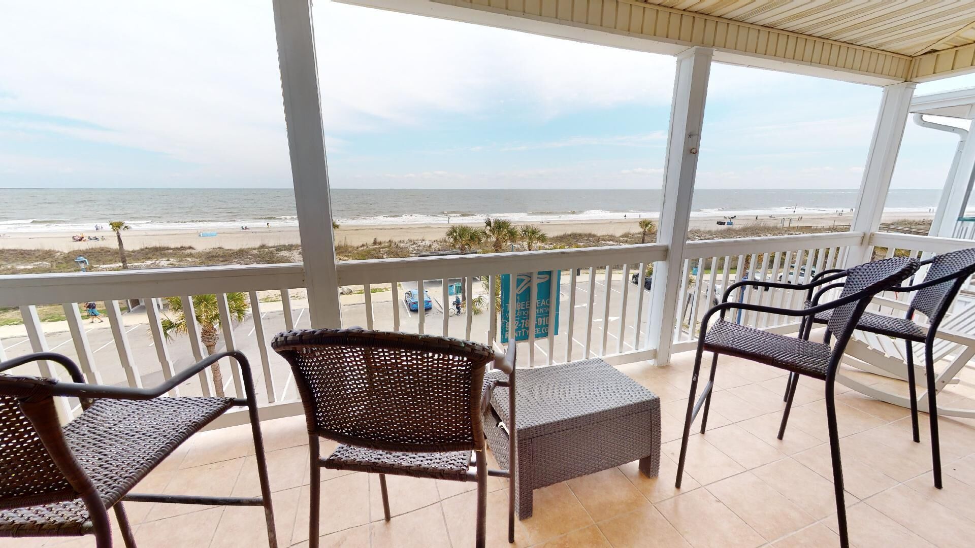 A covered balcony with wicker furniture and a view of the beach.