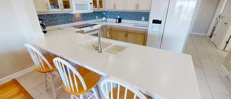 A modern kitchen with a white countertop, two wooden chairs, and a built-in sink.