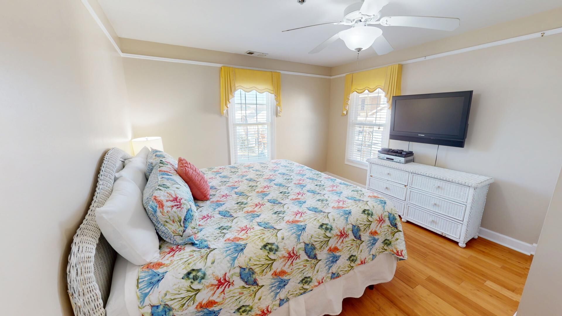 A bedroom with a bed, a TV, a dresser, and a ceiling fan.